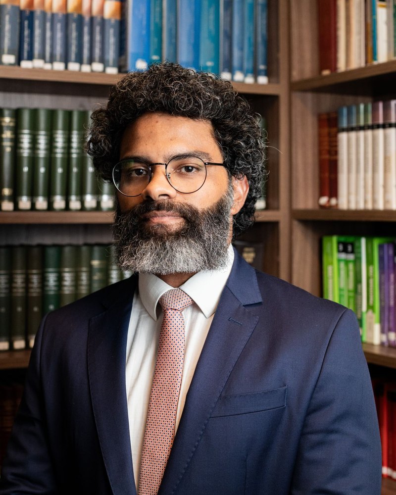 Vinícius Assumpção diante de uma estante de livros